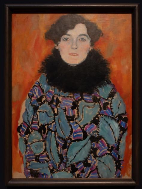 An unfinished Klimt portrait of a woman in a patterned fur-collared coat, the lower canvas left bare.