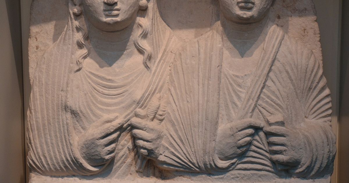 A carved limestone funerary relief from Palmyra showing the busts of a man and a veiled woman side by side, with an inscription cut beside them.
