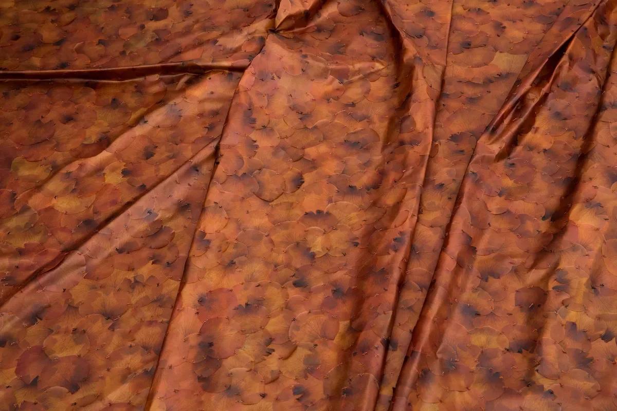 A close view of orange brown fabric gathered into soft folds, its surface flecked with small darker marks.