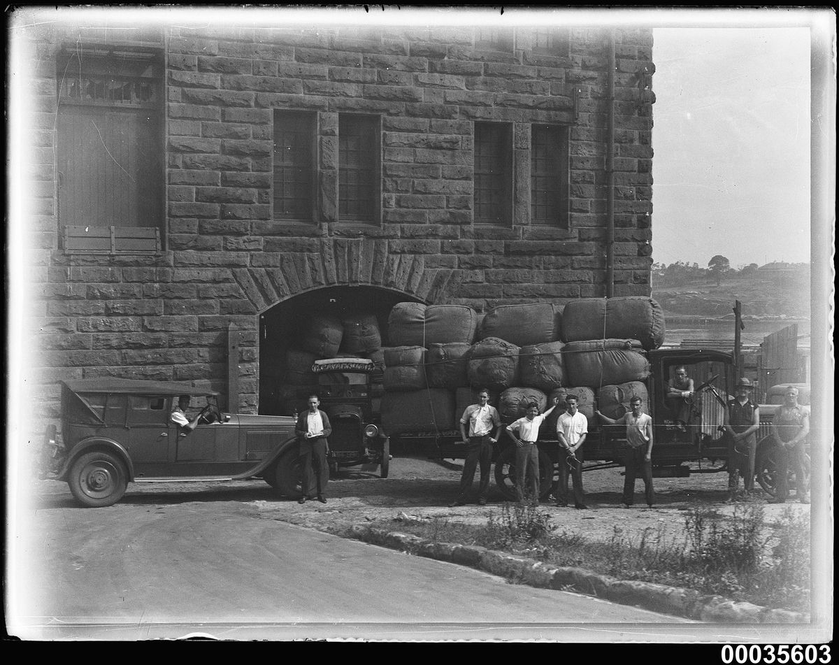 Workers standing with hand trucks loaded with wool bales outside a warehouse.
