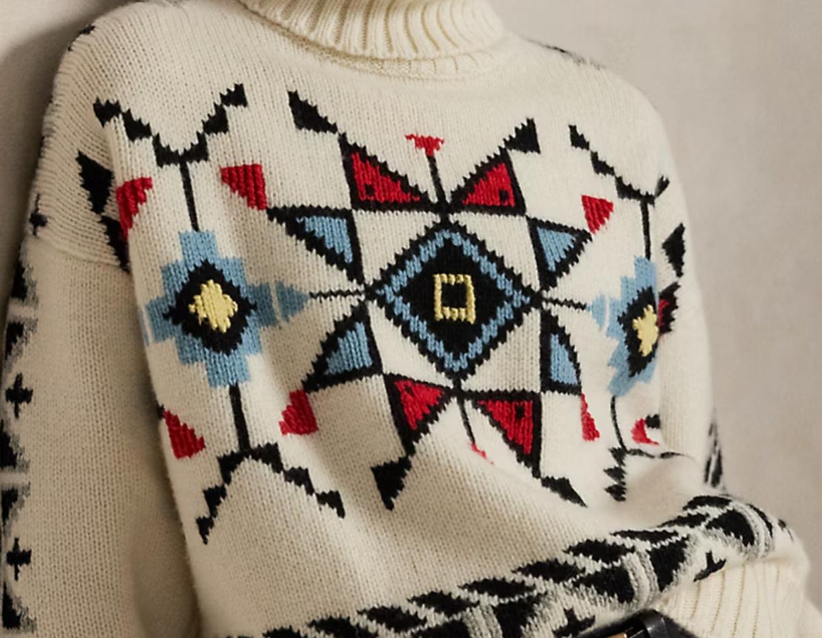 A cream wool sweater with a bold intarsia panel across the chest in black, red, blue and yellow diamond and stepped motifs.