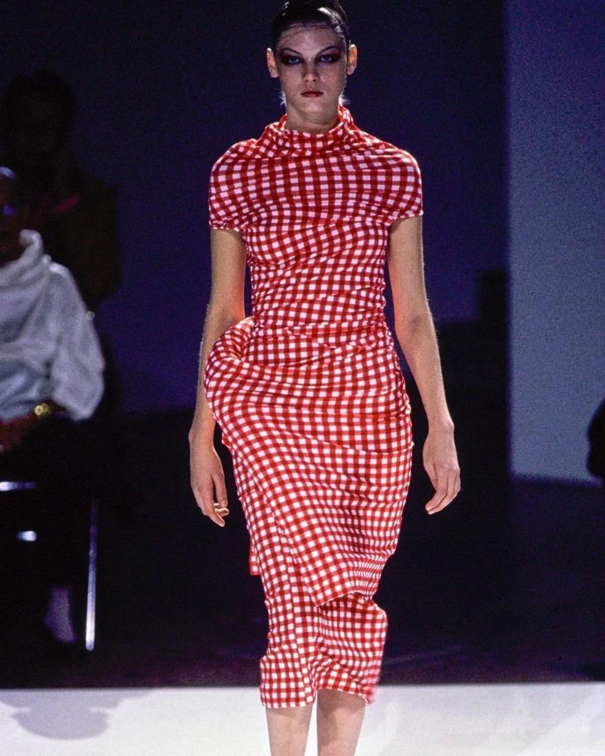 A model on a runway in a red and white gingham dress and matching trousers, the fabric bunched into padded bulges at the hip and back.