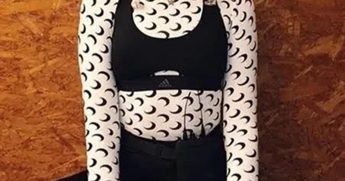 A woman seated on the floor against a chipboard wall wearing a black crop top and leggings layered under a sheer white top and tights printed with repeating crescent moons.