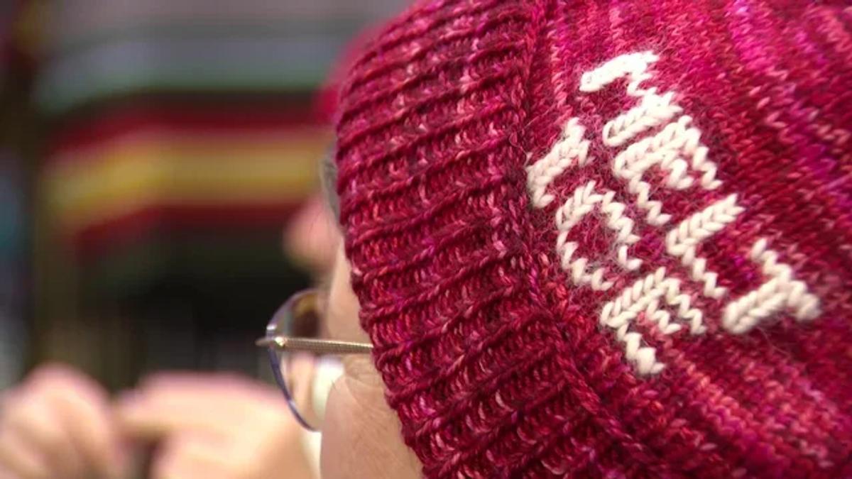 A close view of a deep red knitted hat worn by a person in glasses, the words melt ice knitted into the band in white.