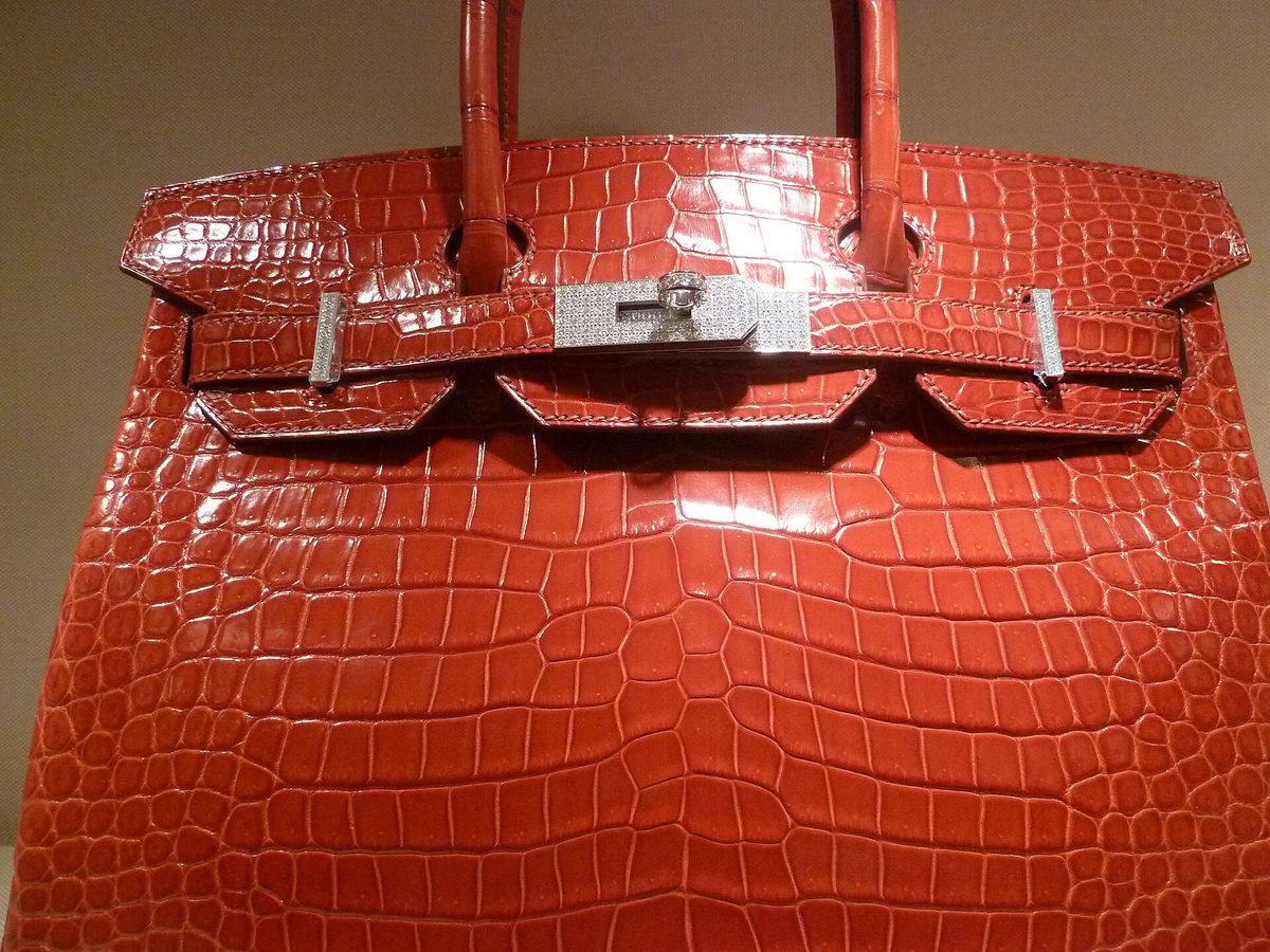 A close view of a red crocodile skin Birkin, the scales pronounced across the body, with a jewelled clasp set into the front strap.