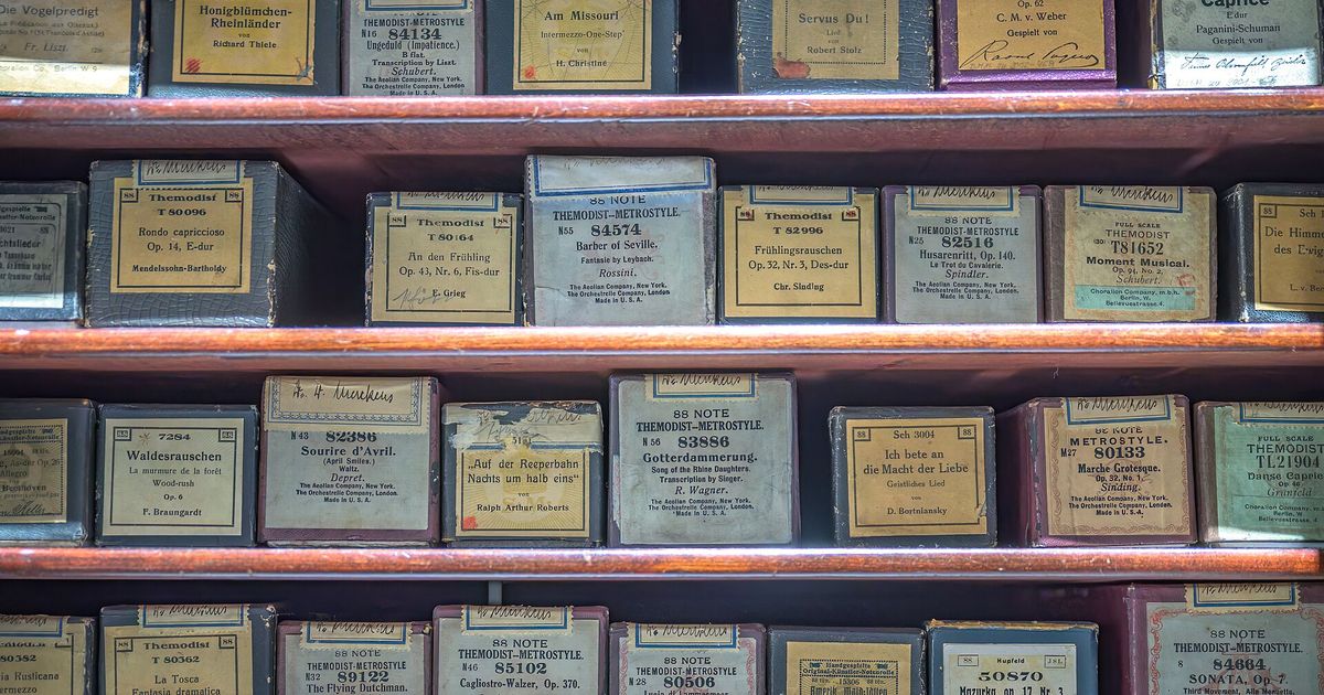 Wooden shelves holding rows of labelled piano roll boxes, each printed with a title, a catalogue number and a composer.