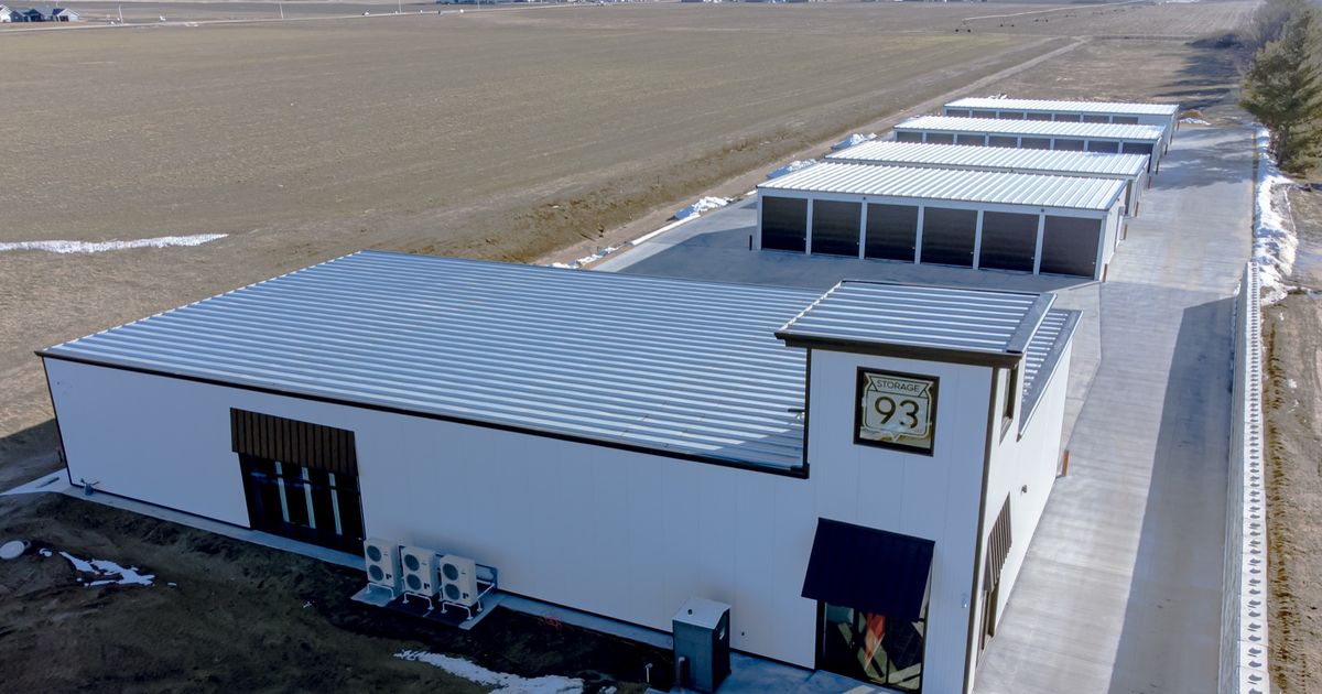 A row of self storage garages with identical roller shutter doors along a paved access lane, each unit numbered and closed.