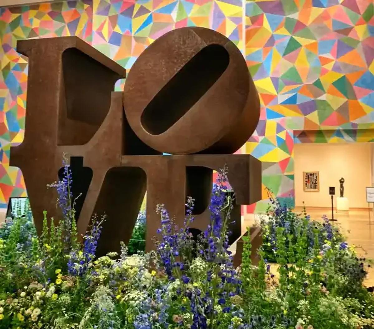  This powerful visual of a Robert Indiana sculpture within the Newfields Indianapolis Museum of Art provides an important sense of place and institutional context for the study. The object here, while instantly recognizable, is transformed through its current installation featuring live floral elements, challenging the static nature of the traditional aesthetic artifact. It reminds us that every object within the museum space is part of a dynamic, evolving narrative that the institution is constantly shaping, reinforcing the vital shift away from aesthetic conformity toward material integrity and contextual resonance discussed in the paper. 