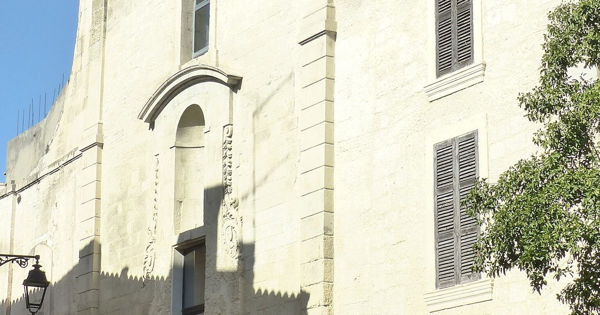 The stone facade of the former Sainte-Croix church in the Roquette district of Arles, seen from the street.