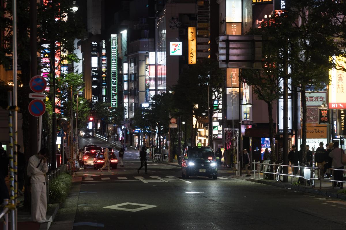 A busy Shinjuku street in Tokyo at night, lit by signage.