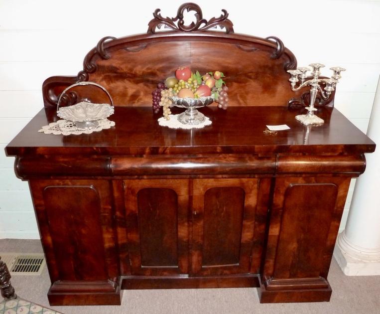 A Victorian mahogany sideboard with carved detailing and a mirrored back, standing against a wall.