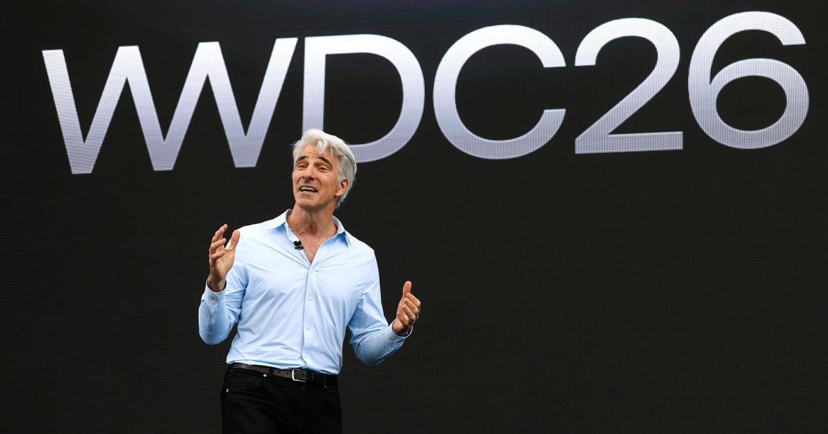 A man in a pale blue shirt speaking on a dark stage in front of a large screen reading WWDC26.