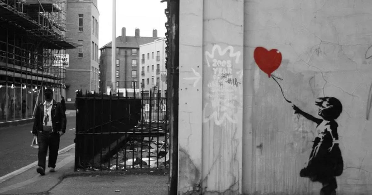 A two panel black and white street scene: a man walking past a hoarding and scaffolding, and beside it the stencil of a girl reaching for a heart shaped balloon, the balloon printed in red.