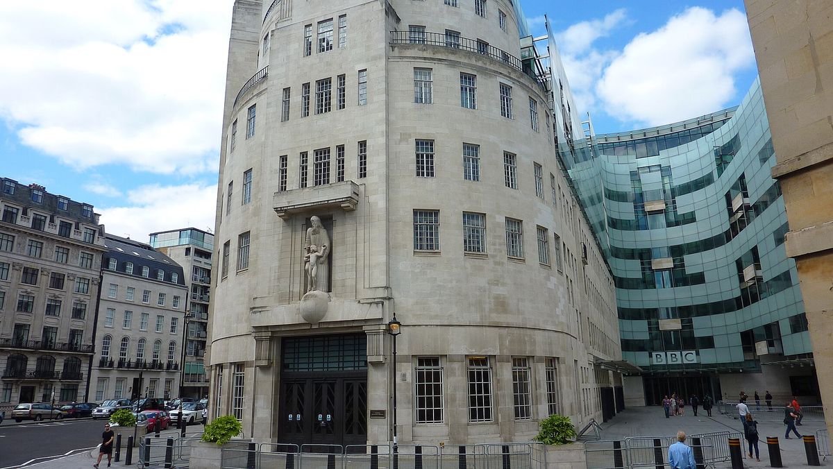 BBC Broadcasting House on Portland Place, London: a curved white stone building with a clock face and mast, seen from the street.
