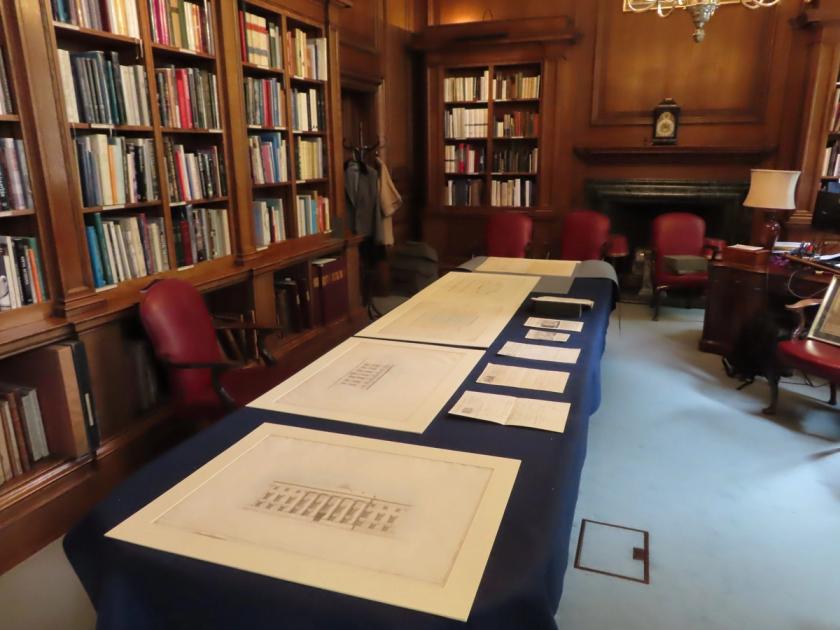 The library at Goldsmiths' Hall, wood panelled with full bookshelves, and archival drawings and documents laid out along a long table covered in dark blue cloth.