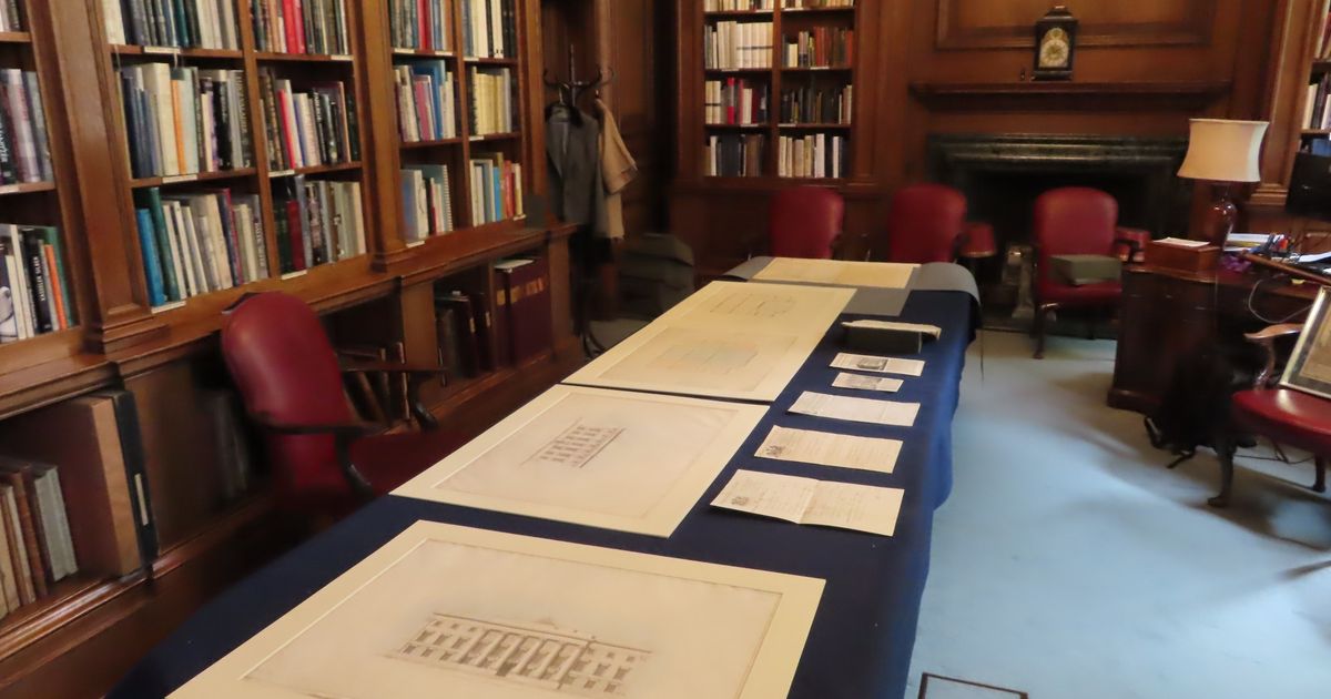 The library at Goldsmiths' Hall, wood panelled with full bookshelves, and archival drawings and documents laid out along a long table covered in dark blue cloth.
