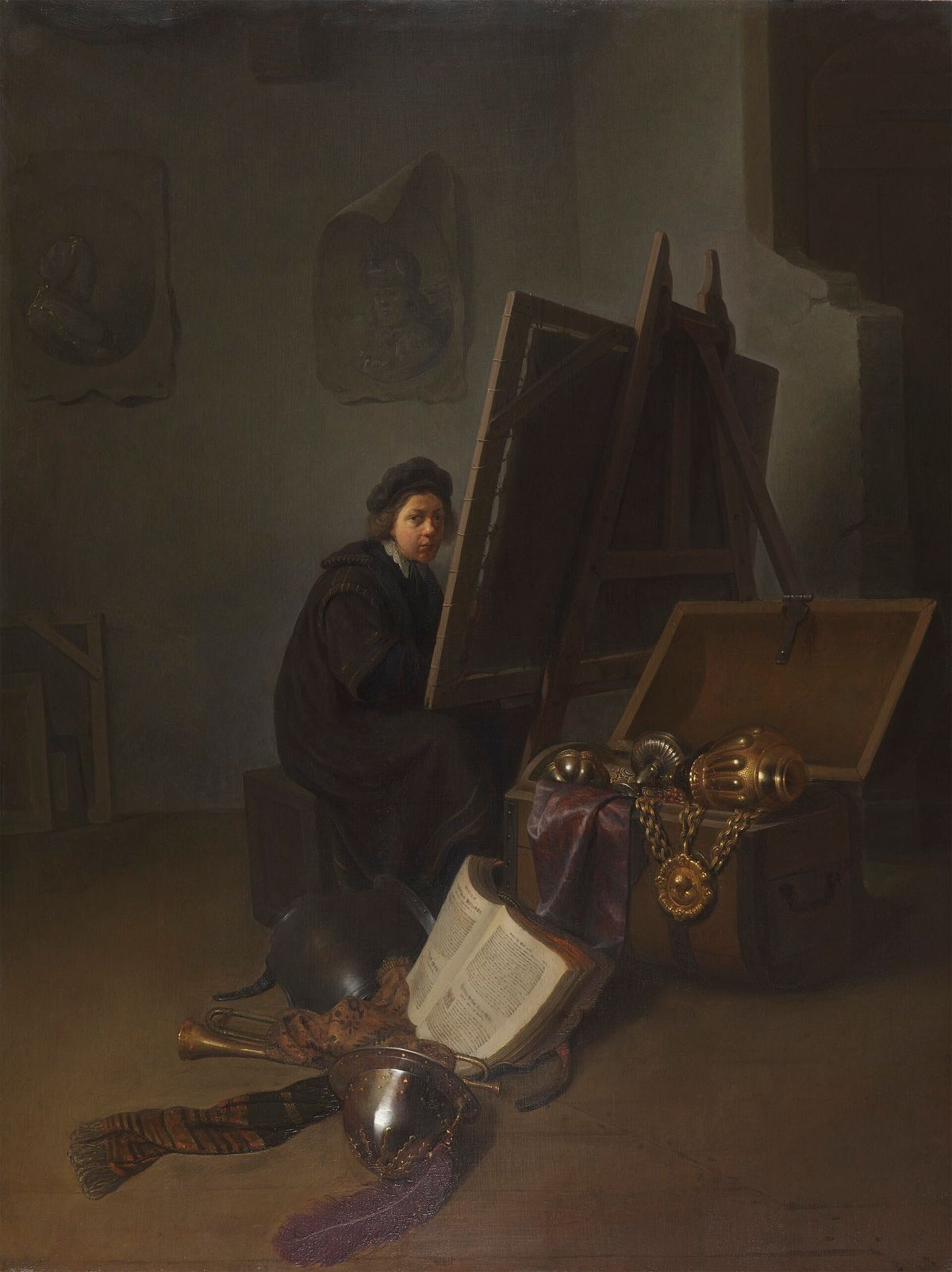 An Artist in His Studio: a seventeenth century painting of a man seated at work in a shadowed room hung with the tools of his trade.