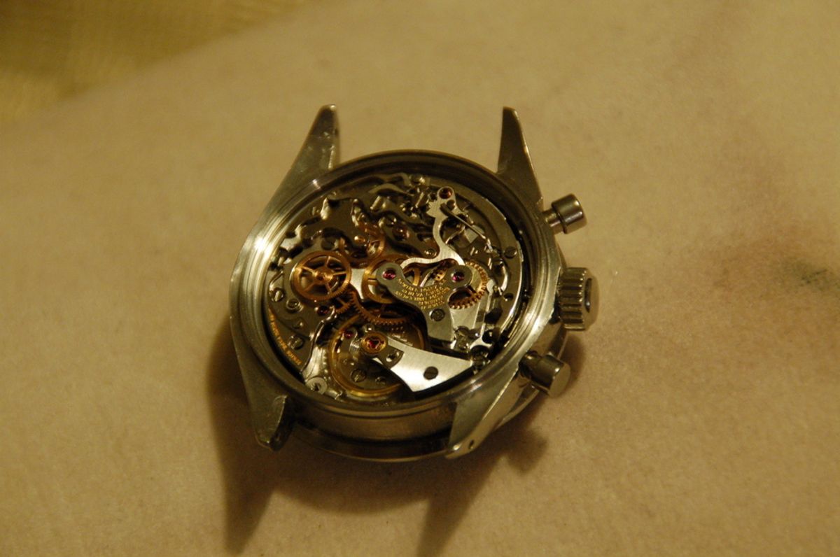 An opened chronograph case showing the movement in situ, the caseback removed and the bridges and screws visible.