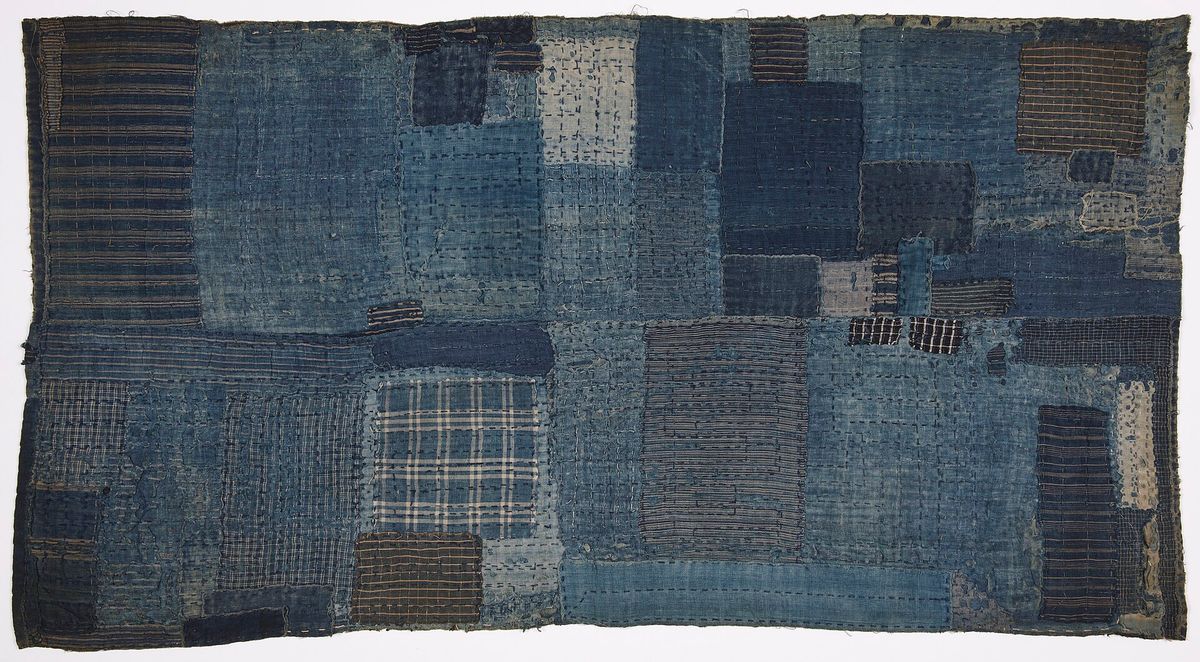 A rectangular indigo textile assembled from dozens of patched rectangles in many weaves, stitched all over, frayed at the edges.