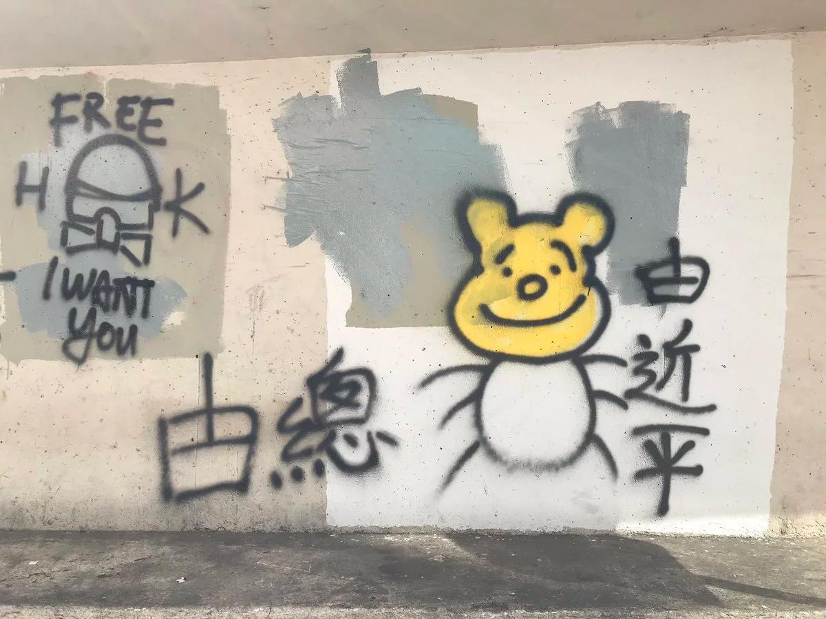 A concrete wall sprayed with a cartoon bear, Chinese characters and the words free and I want you, part of the surface painted over in grey.