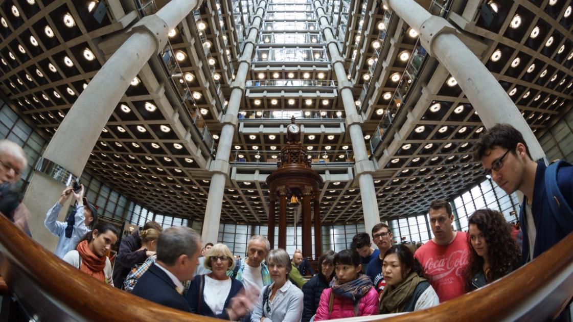 The underwriting room at Lloyd's of London, a tall open hall of desks across several galleried levels beneath a high atrium, with underwriters seated at boxes.