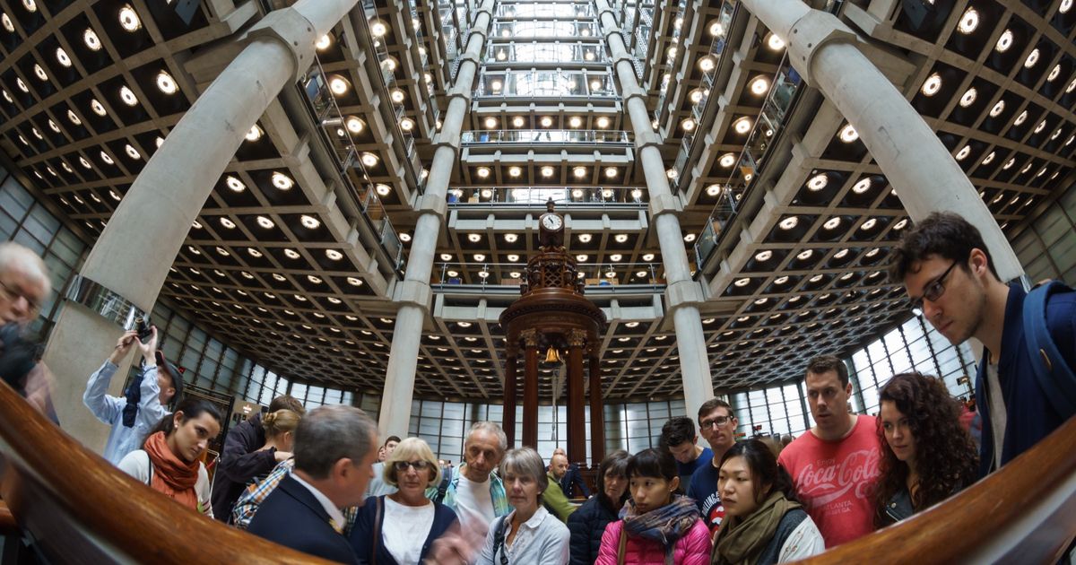 The underwriting room at Lloyd's of London, a tall open hall of desks across several galleried levels beneath a high atrium, with underwriters seated at boxes.