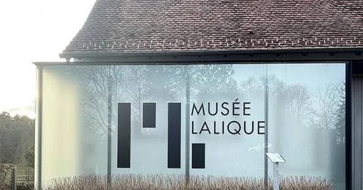 A low museum building with a tiled roof and full height glass walls, Musee Lalique lettering across the facade and clipped hedges in front.