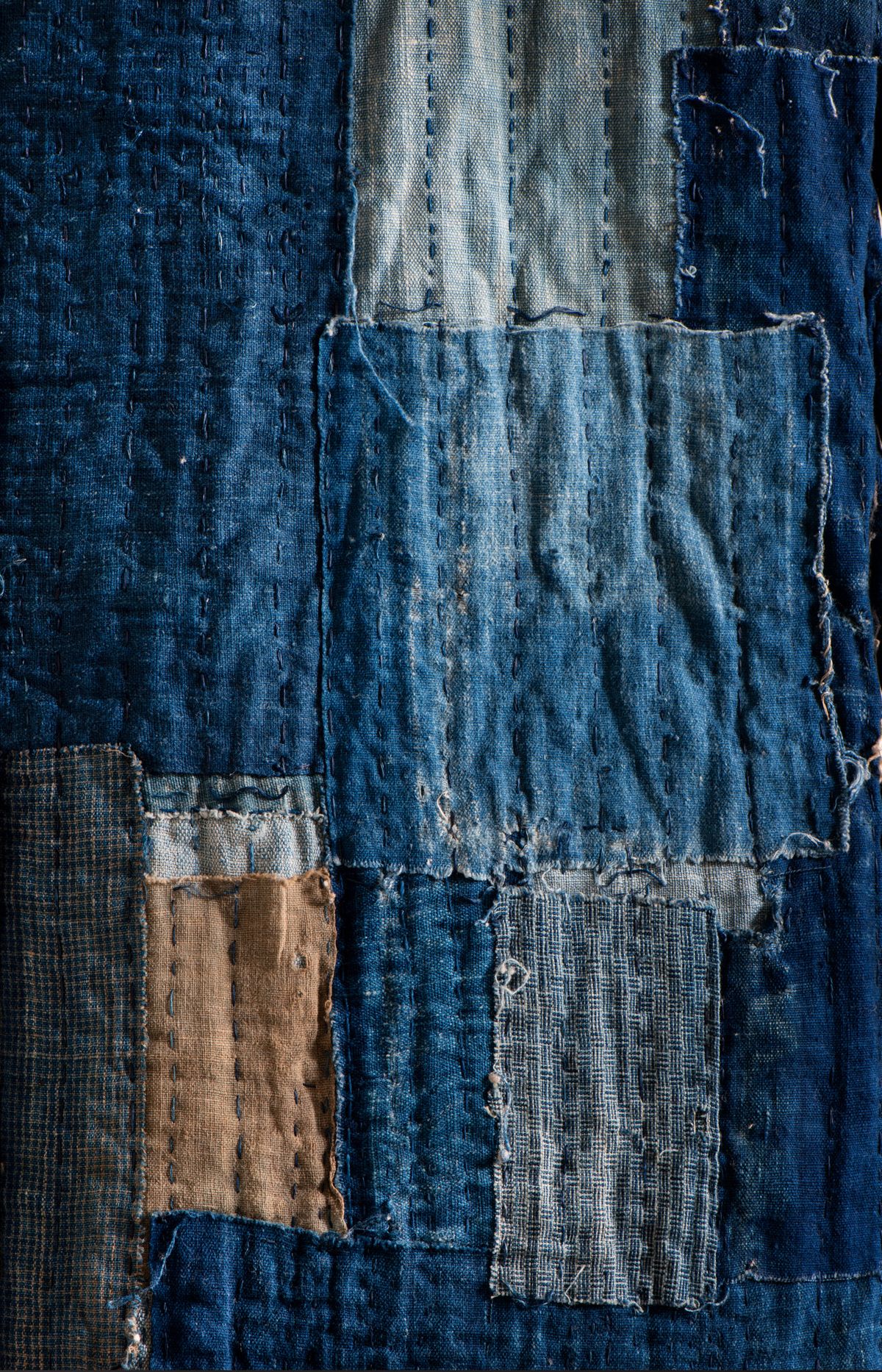 A Japanese boro textile assembled from many indigo patches held together by rows of white sashiko stitching.