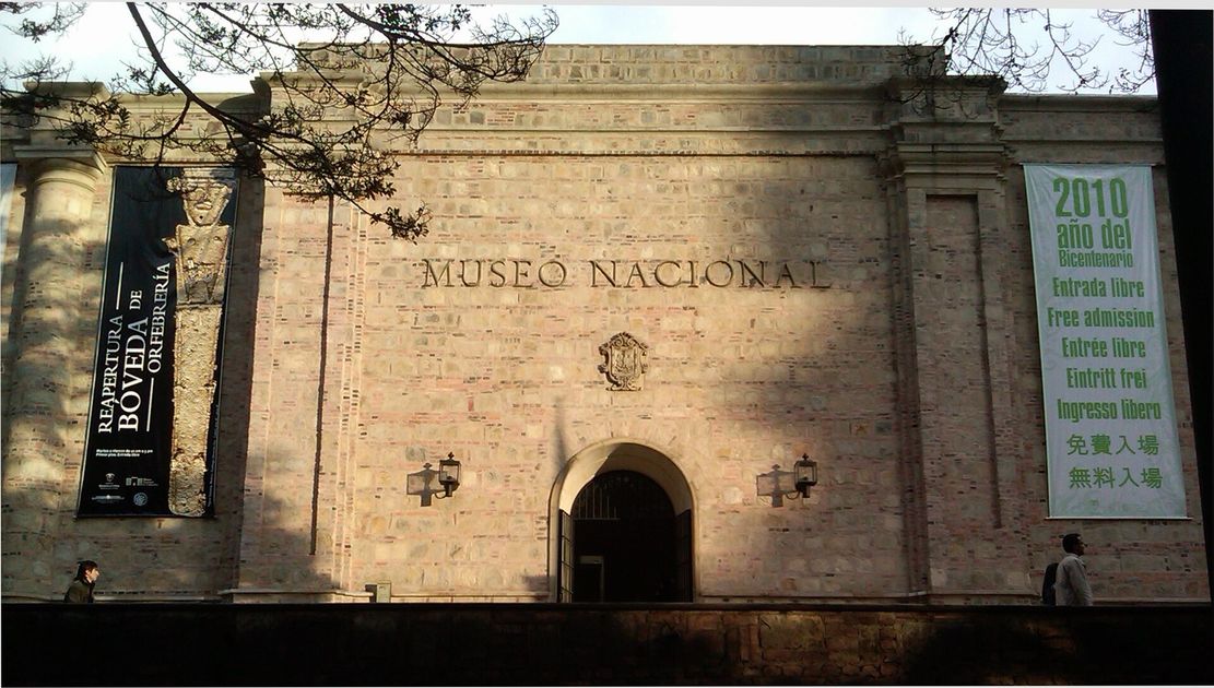 The stone front of the Museo Nacional de Colombia, the words MUSEO NACIONAL carved across it above an arched doorway, with hanging banners either side.