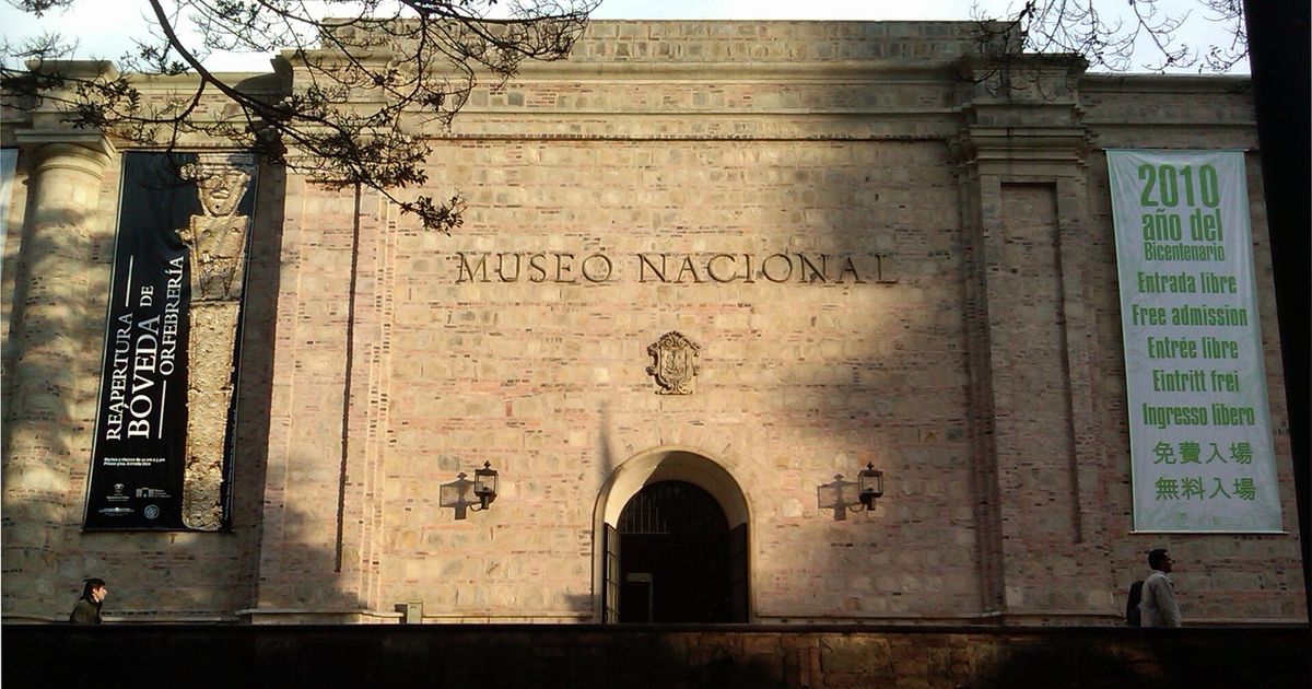 The stone front of the Museo Nacional de Colombia, the words MUSEO NACIONAL carved across it above an arched doorway, with hanging banners either side.