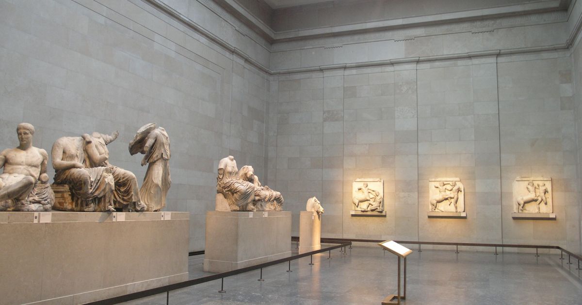 A long top-lit stone gallery with carved marble figures on low plinths along the left wall and relief panels mounted along the right.