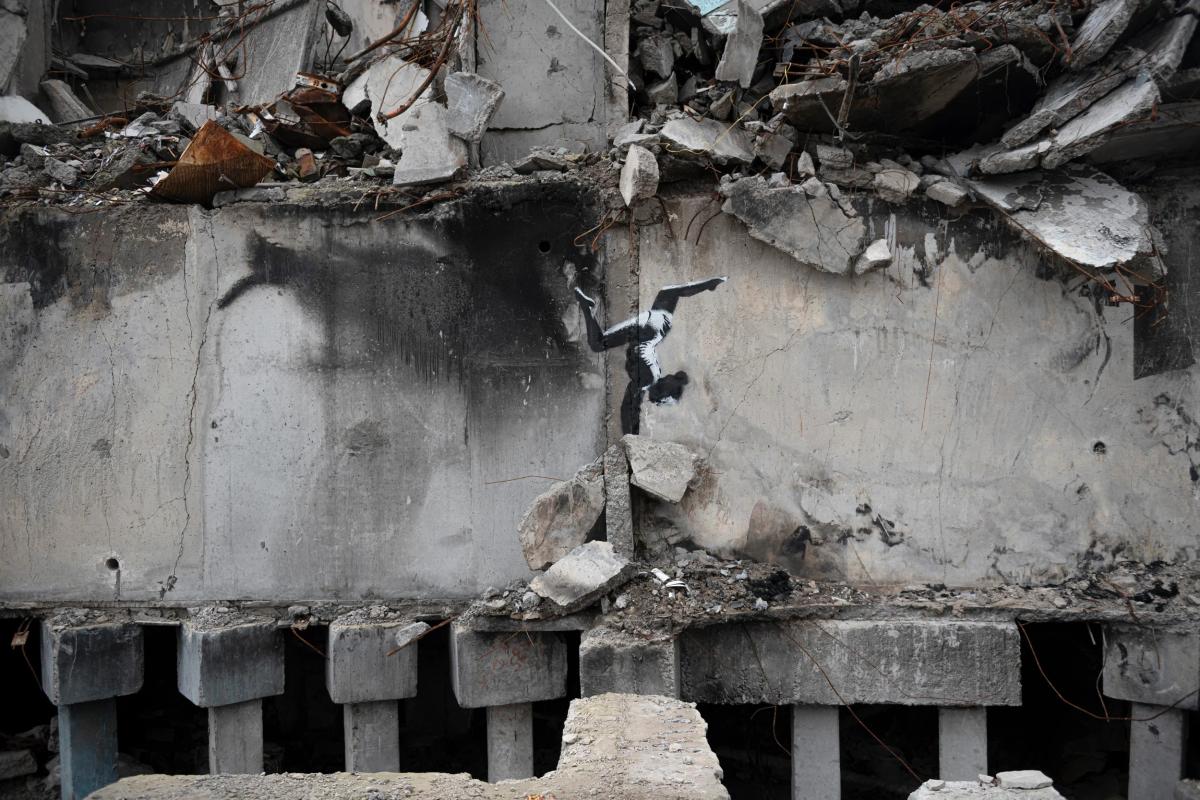 A bombed concrete building with its upper floors collapsed, and on the intact lower wall a small stencilled figure balanced amid the rubble.
