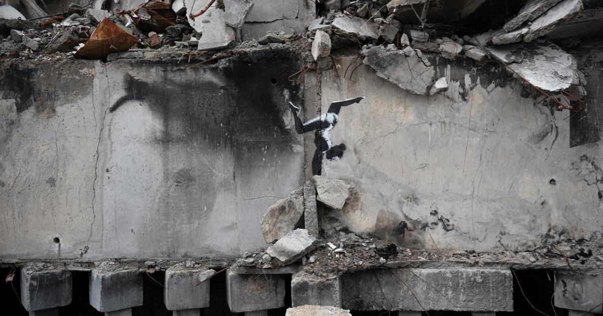 A bombed concrete building with its upper floors collapsed, and on the intact lower wall a stencil of a figure balanced on the rubble.