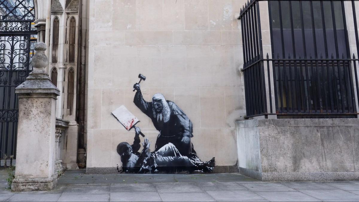 Banksy’s unsanctioned street work, like this stencil depicting a destructive attack on a person holding a book, demonstrates the ongoing potency of clandestine authorship and viral documentation, a key contemporary precedent for TSH's methods of spectacle and confrontation.