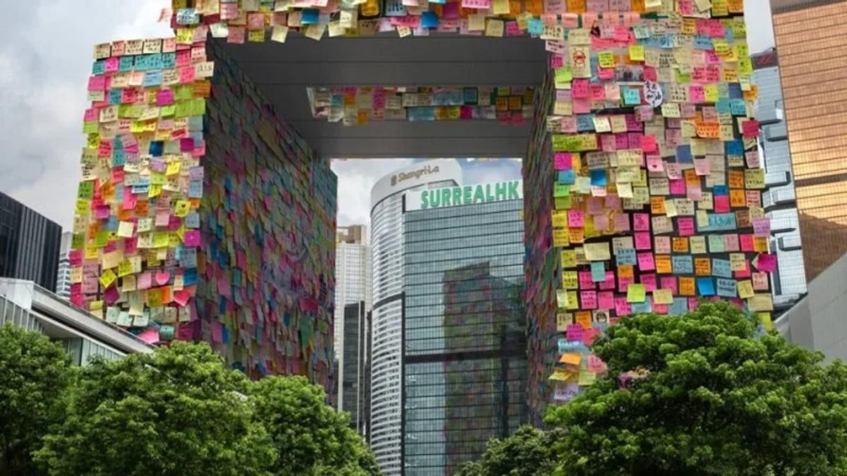 A public stairway and wall covered from top to bottom in thousands of coloured sticky notes, city towers visible beyond.