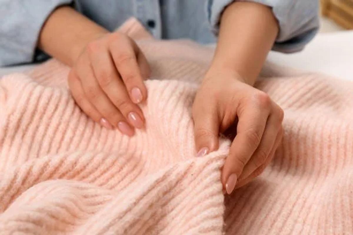 Two hands resting on a folded pale pink ribbed knit, fingers spread across the surface of the wool.