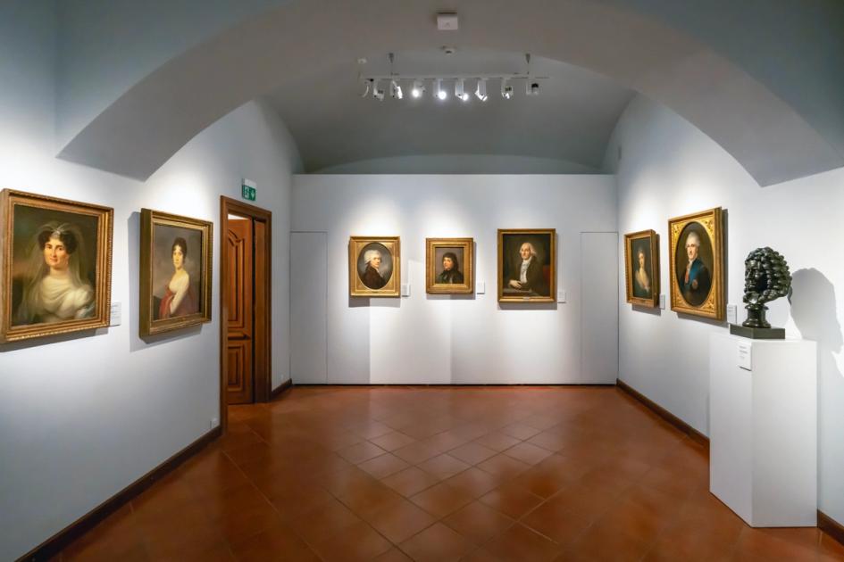 The interior of an art gallery, its walls hung with framed works.