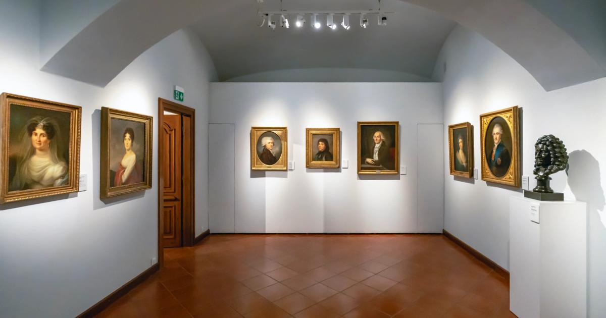 The interior of an art gallery, its walls hung with framed works.