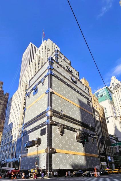 The Louis Vuitton construction shed at Fifth Avenue and East 57th Street, built to resemble a stack of monogrammed grey canvas trunks with black edging, metal corner protectors, buckles and handles, rising sixteen storeys against a clear sky.