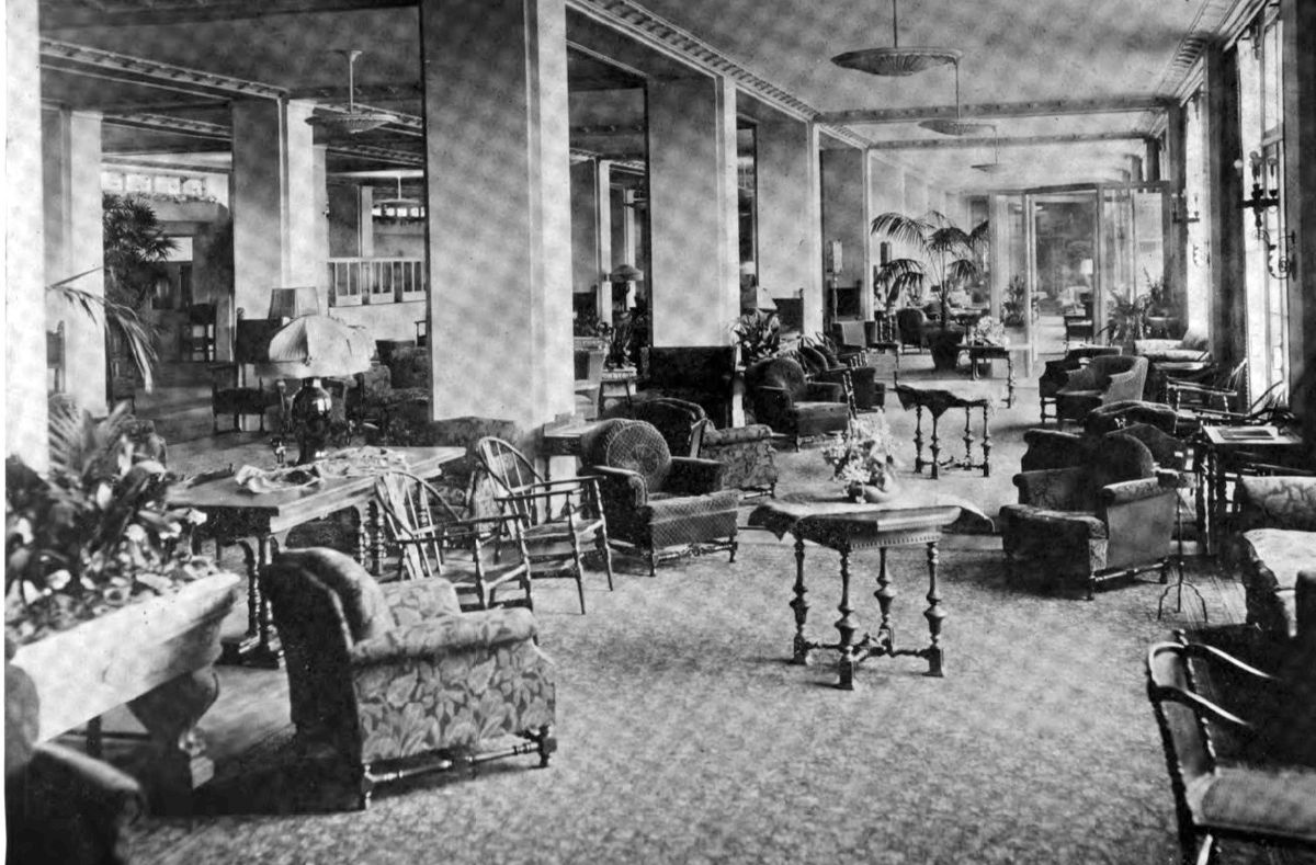The lobby of a grand 1920s hotel, with columns, patterned carpet and arranged seating.
