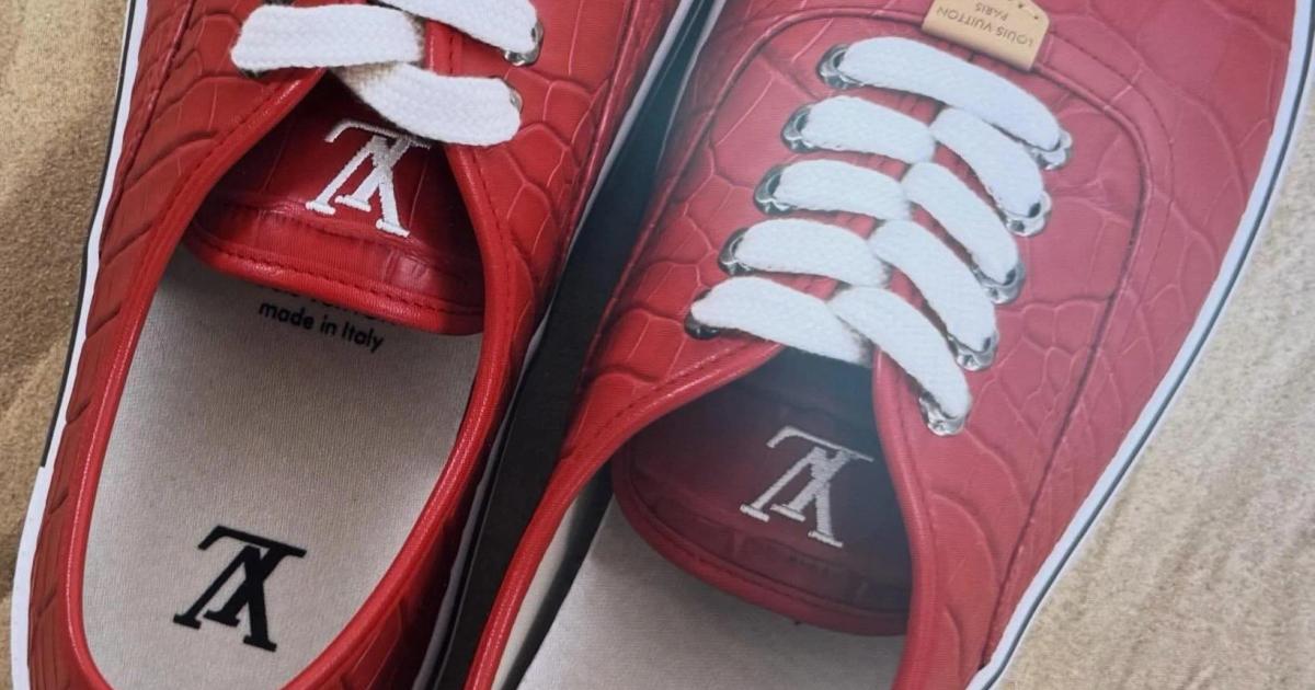 A pair of red crocodile embossed low top sneakers with white laces and monogram initials on the toes, photographed from above on sand.