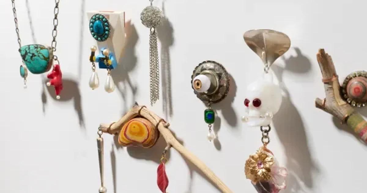 A wall hung with handmade jewellery: pendants and earrings assembled from turquoise, shells, coral, glass, bone and found metal fragments on fine chains.