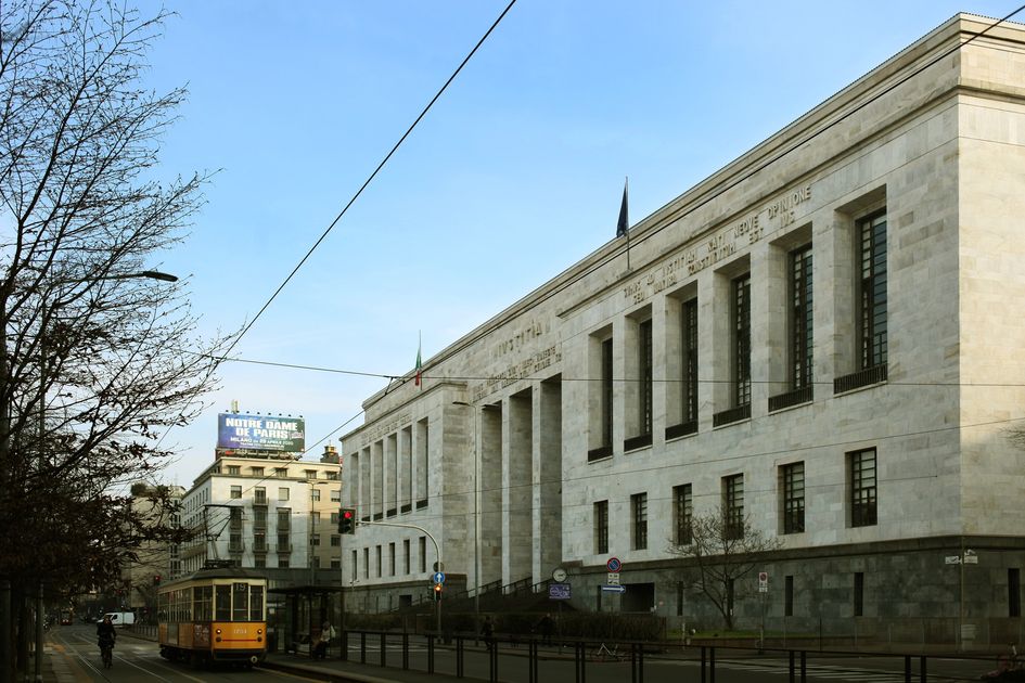 The Palazzo di Giustizia in Milan, a monumental white stone courthouse by Marcello Piacentini, seen along the street with a yellow tram passing.