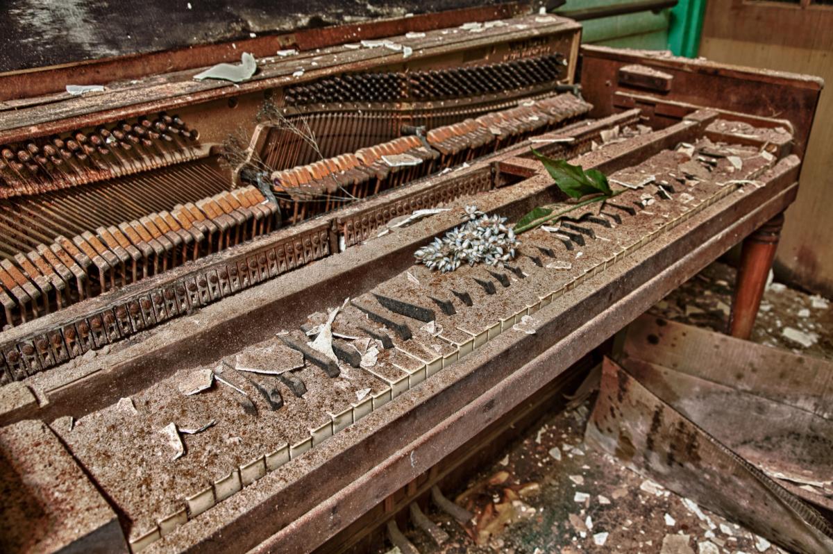 An abandoned upright piano standing outdoors, its case weathered, with flowers left on the lid.