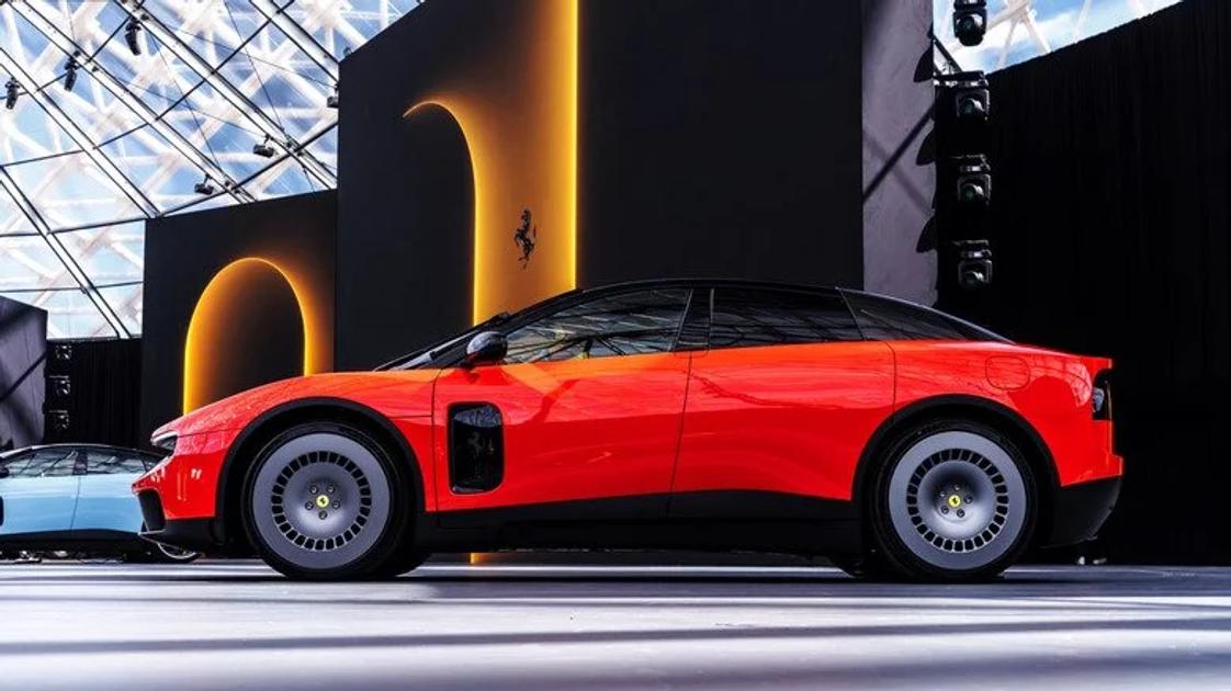 A red sports car photographed in profile on a show stand, a black backdrop behind it carrying a prancing horse emblem and glass roof structure above.
