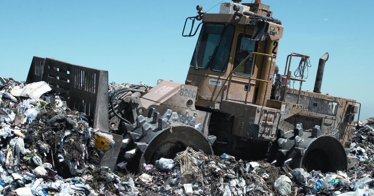 A heavy landfill compactor working across a spread of refuse at a waste site.