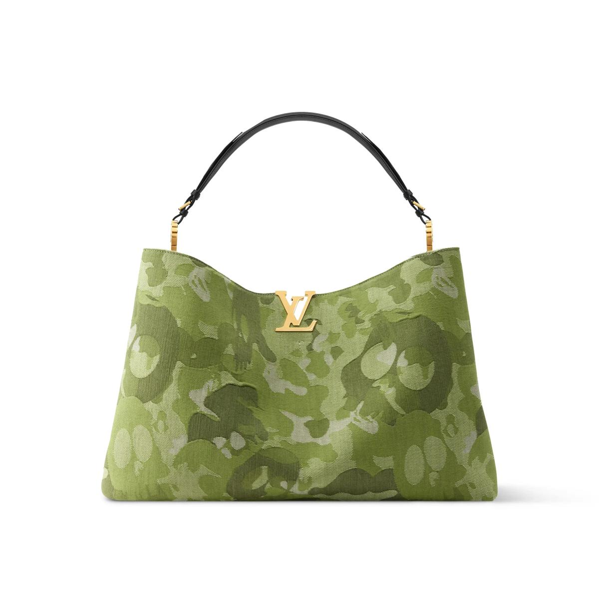 A soft olive green handbag printed with a pale camouflage pattern, a slim black top handle and a gold monogram charm on the front.
