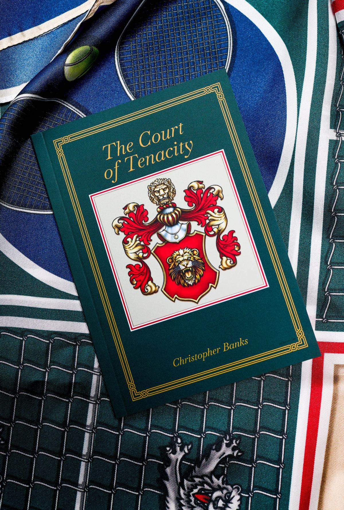 The cover of The Court of Tenacity by Christopher Banks, a red and gold lion crest framed in gold on dark green, lying on the printed scarf.