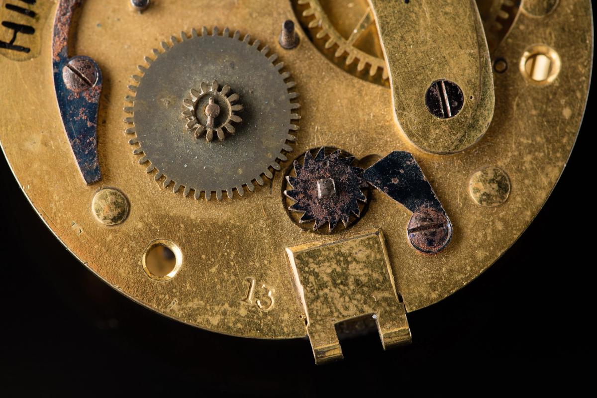 A macro photograph of an antique pocket watch movement, the number 13 stamped into the plate between the wheels.
