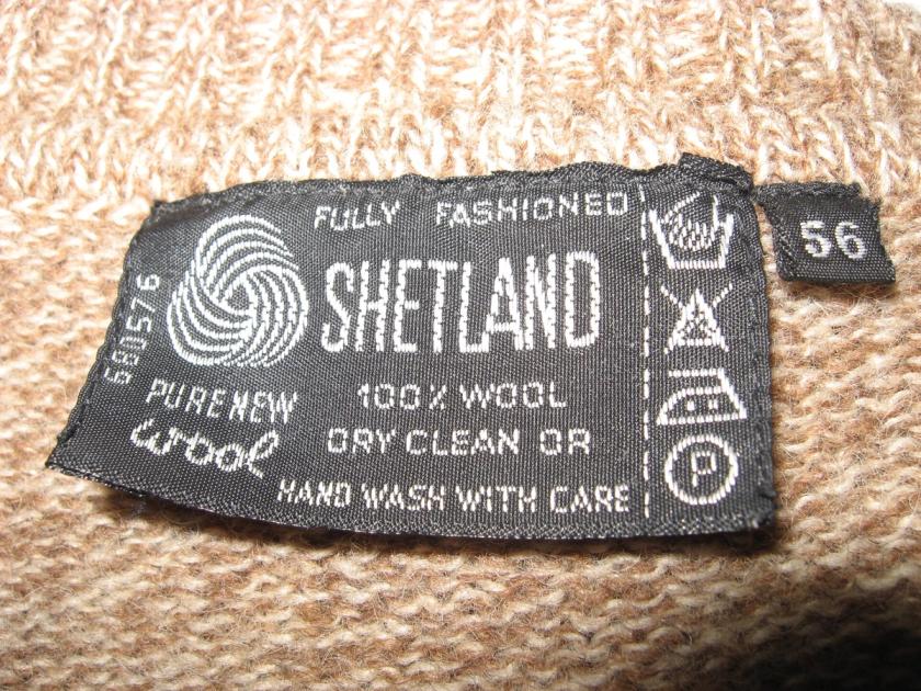 A sewn-in woven garment label reading 100 percent wool with care symbols, the object’s minimal testimony before the digital product passport.